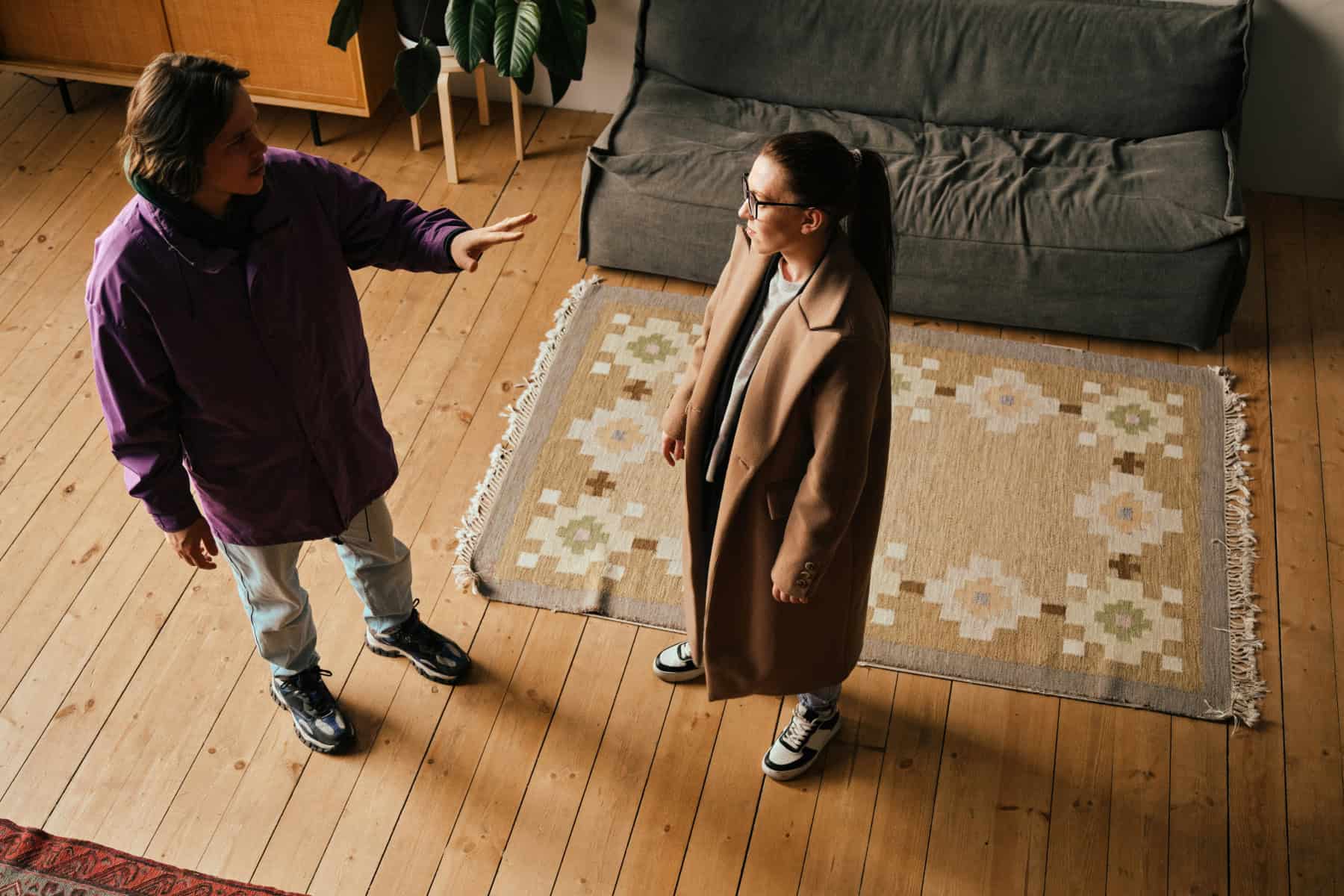 Two people stand facing each other in a living room during a tense conversation; one gestures with an outstretched hand while the other listens.
